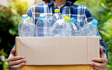 Mujer cargando botellas de plástico en caja cartón