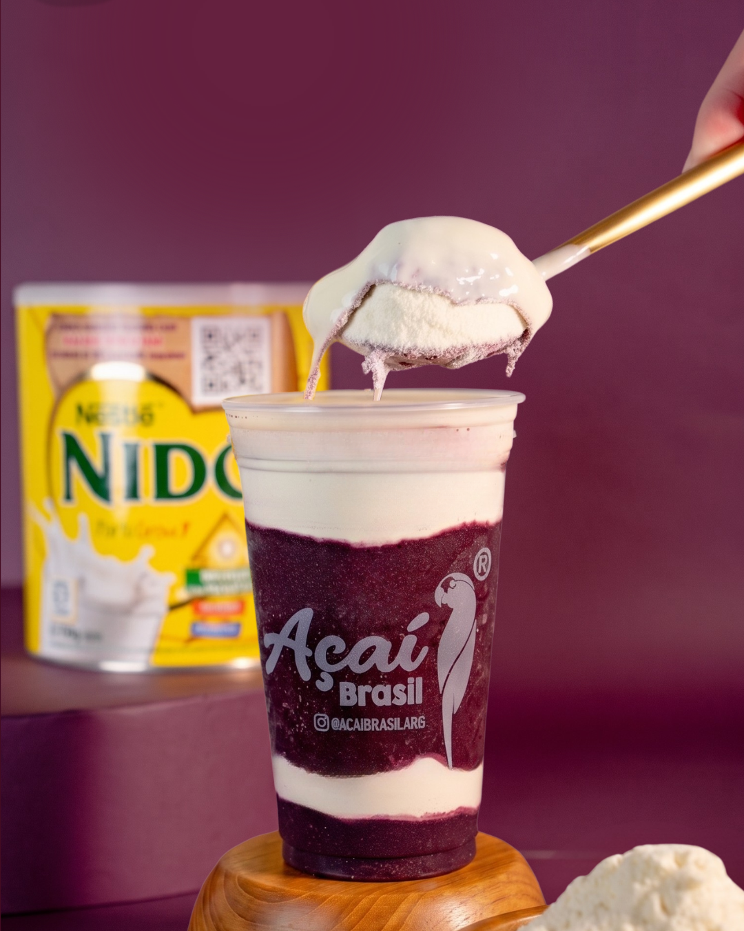 Vaso de açaí con capas de crema elaborada con NIDO®, junto a una cuchara con una porción del producto.